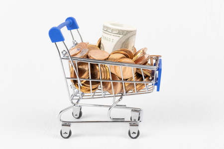 metal chrome shiny shopping trolley on wheels with gold coins and paper dollars isolated on white backgroundの写真素材
