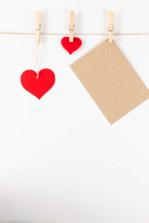 three wooden clothespins hang on a rope on a white background and hold a heart and an envelope. flat layの写真素材