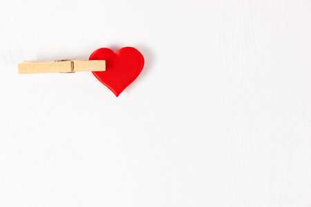 red heart clamped in a linen wooden clothespin on the background of a white wooden table. close-up....
