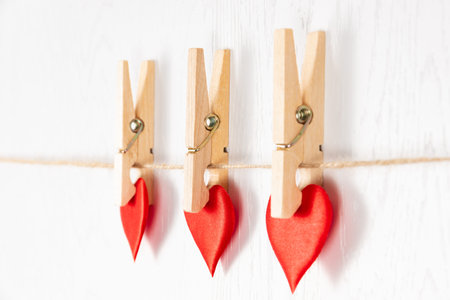 three wooden clothespins with a metal spring hang on a rope on a white background and hold a heart....