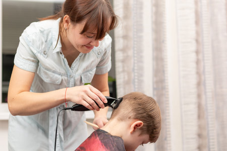young mom hairdresser cuts her baby boy at home with hair clipper during quarantine. selective...
