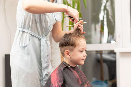 caring female hands of a mother with a comb and scissors make a fashionable haircut for her son at home during the second lockdown. selective focusの写真素材
