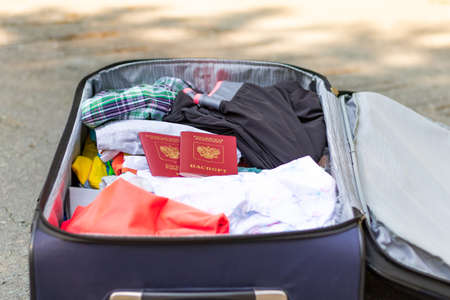 An open suitcase with things and two passports lies on the road on a sunny summer day. Selective focusの写真素材
