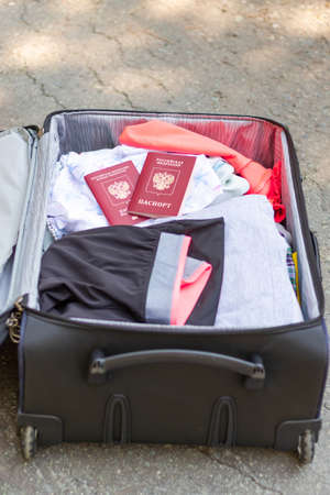 An open suitcase with things and two passports lies on the road on a sunny summer day. Selective focusの写真素材