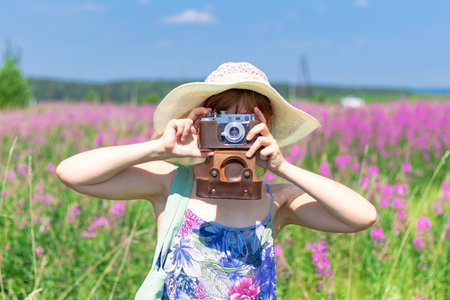 Portrait of a young woman with a camera in a hat in a field of red flowers on a hot summer day....
