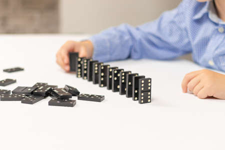 Six year old cute boy plays dominoes at home on a white wooden table. Selective focus. Close-upの写真素材