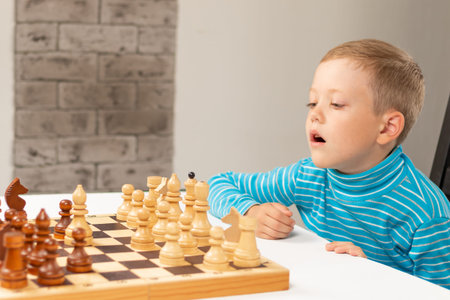 Cute seven year old child boy playing chess at home on a white wooden table. Selective focus....