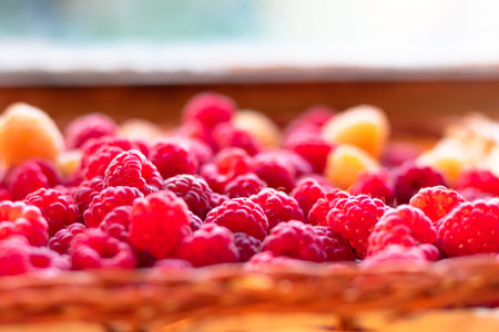 Fresh fragrant tasty red and yellow raspberries in a basket on a wooden background. Selective focus....