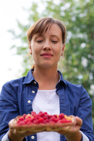 A beautiful young woman in a blue shirt holds a basket of fresh fragrant raspberries in her hands...