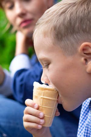 Preschooler boy with mom eating ice cream on the porch of a house in the village on a summer sunny day. Selective focus. Portraitの写真素材