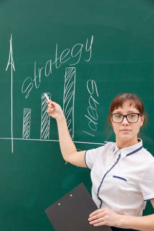 a young woman business coach in a white blouse and glasses shows with her hand a diagram of building a business on a graph. office workの写真素材