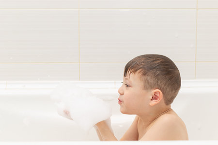 a preschool boy washes in a light white bathtub and plays with lather. close-up portrait