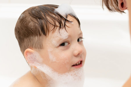 a preschool boy washes in a light white bathtub and plays with lather. close-up portrait