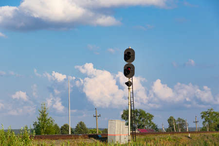 Traffic light on the railway in the village against the background of the forest and blue sky with white clouds on a bright sunny summer day. Close-upの写真素材