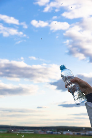 A woman's hand raises a highly transparent bottle of pure mineral water. Splashes are flying against...