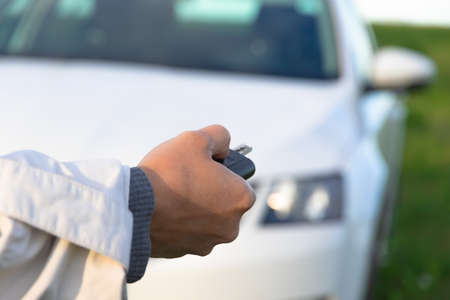 A woman's hand holds the key to a new white car and opens it on a bright sunny summer day against a background of green grass. Selective focus. Close-upの写真素材