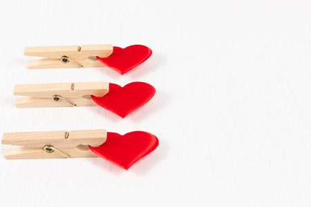 three wooden clothespins with a metal spring hold a red heart on a white wooden table background....