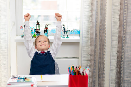 Cute boy first grader in school uniform at home during a break fooling around while sitting at his...