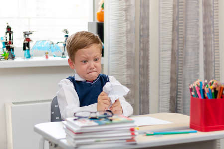 Cute boy first grader in school uniform at home during a break fooling around while sitting at his desk. Selective focus. Close-up. Portraitの写真素材