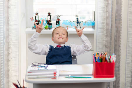 Cute boy first grader in school uniform at home during a break fooling around while sitting at his desk. Selective focus. Close-up. Portraitの写真素材