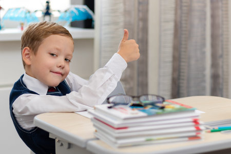 Cute boy first grader in school uniform at home during a break fooling around while sitting at his...