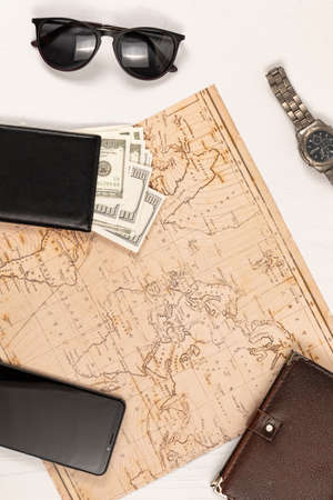 world map, smartphone, black leather wallet with money, diary, sunglasses and a watch on a white wooden table. view from aboveの写真素材