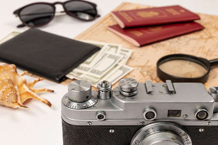 world map, two passports, a magnifying glass, money in a black leather wallet, an old film camera, sunglasses and a shell on a white wooden table. selective focus. inscription - passport Russian Federationの写真素材