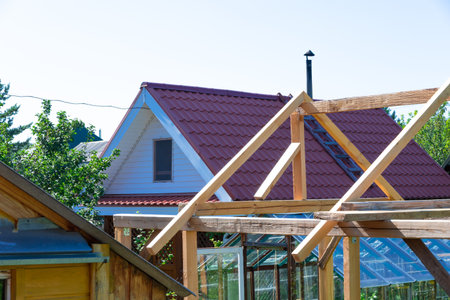 Roofs of wooden houses and greenhouses in the village against the background of blue sky and green...
