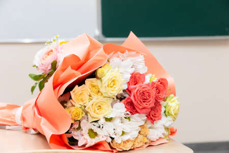 A bouquet of beautiful bright flowers on a school desk on September 1 against the background of a school board. Selective focus. Close-upの写真素材