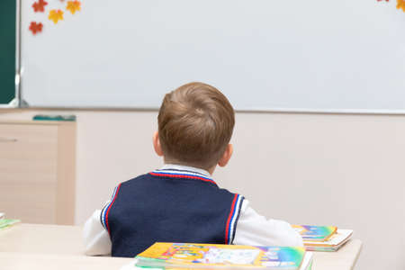 A first-grader boy at his desk in the classroom on the day of knowledge on September 1 at school in the lesson against the background of a white board. Selective focus. Close-upの写真素材