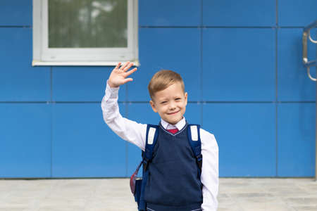 A cute first grader boy in a school uniform with a schoolbag goes to school on a sunny autumn day. Celebration on September 1st. Knowledge day. Selective focusの写真素材