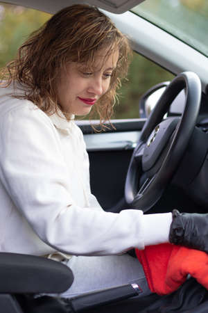 A beautiful young woman driver in a white jacket and black gloves wipes the dust in the car interior with a red rag on a bright warm autumn day. Selective focus. Portraitの写真素材