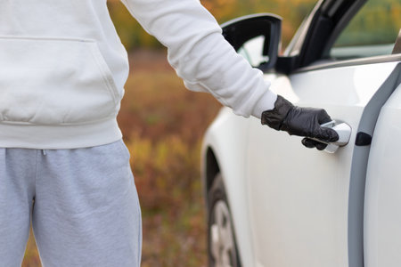 A man in a white sweater and black gloves opens the car door to steal him on a warm autumn day. Selective focus. Close-upの写真素材
