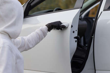 A man in a white sweater and black gloves opens the car door to steal him on a warm autumn day. Selective focus. Close-upの写真素材