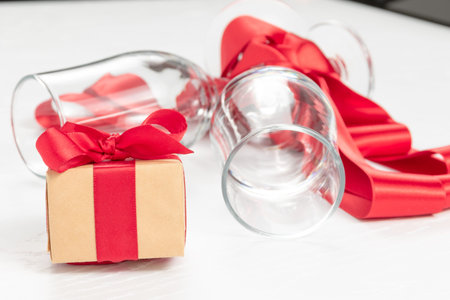 two champagne glasses, a gift box and a red silk ribbon on a white wooden table. close-up