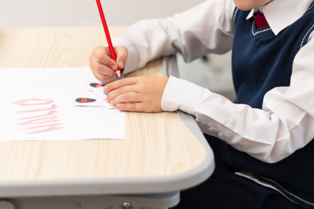 A first grader boy draws a postcard for the holiday of halloween with a red bright pencil on a white sheet of paper while sitting at a white table. Selective focus. Bokehの写真素材