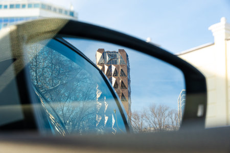 The view from the car through the side rearview mirror to the golden crystal tower against the blue...