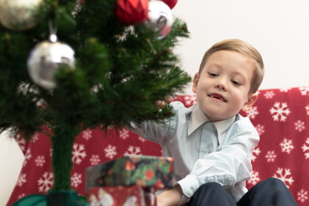 A seven-year-old boy is happy with gifts for the New Year against the background of a New Year tree sitting on a warm blanket. Selective focus. Portraitの写真素材