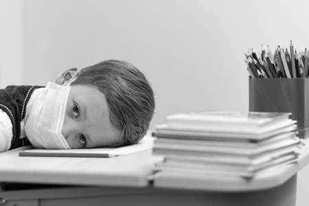 A cute first grader boy in a school uniform at his desk wearing a protective medical mask during the coronavirus pandemic. Selective focus. Close-up. Portraitの写真素材