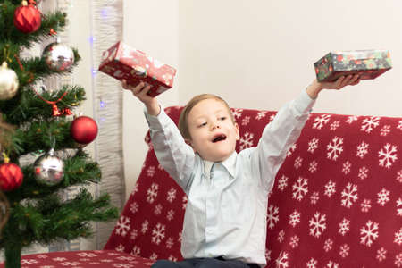 A seven-year-old boy is happy with gifts for the New Year against the background of a New Year tree sitting on a warm blanket. Selective focus. Portraitの写真素材