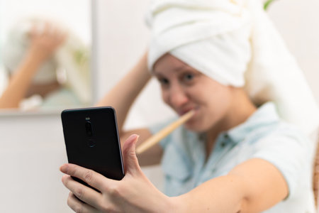 A young pretty woman with a towel on her head in a bright bathroom with a toothbrush and a...