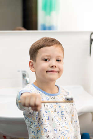 A cute seven year old boy in pajamas with a bamboo toothbrush brushes his teeth before going to bed at home in the bathroom. selective focus. Portraitの写真素材