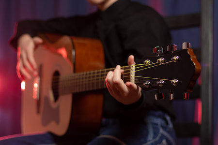 A teenager guy in a black shirt with a guitar in his hands on a purple dark background with red illumination on the stage. selective focus. Portraitの写真素材