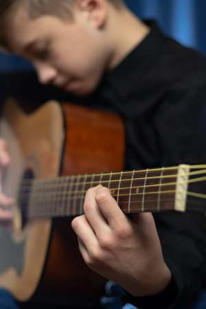 A teenager guy in a black shirt plays the acoustic guitar at a concert on a blue background. hobby....