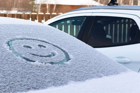 Drawing of a smiling face on a snowy rear window of a car on a winter sunny day. selective focus. close-upの写真素材