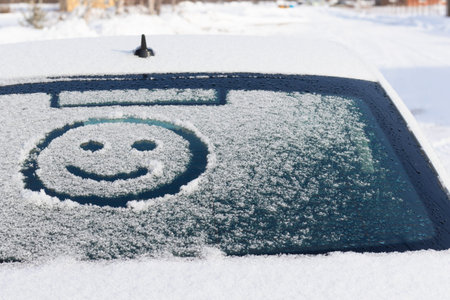 Drawing of a smiling face on a snowy rear window of a car on a winter sunny day. selective focus. close-upの写真素材