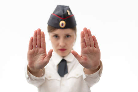 Beautiful young female Russian police officer in dress uniform shows a stop sign with her hands on a white background. selective focus. Portraitの写真素材