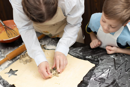 Mom and son are cutting out molds for baking sweet cookies from puff pastry on a black wooden table...