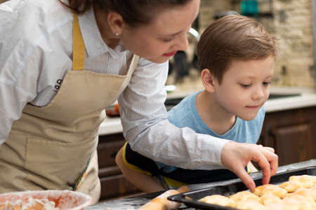 Mom and son try sweet puff pastry lying on parchment on a baking sheet at home in the kitchen. Nearby lies a rolling pin and a bowl. selective focus. portrait. close-upの写真素材