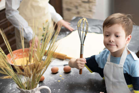 Mom and son in aprons roll out puff pastry for baking on a black kitchen table sprinkled with flour at home with a wooden rolling pin. selective focus. close-upの写真素材
